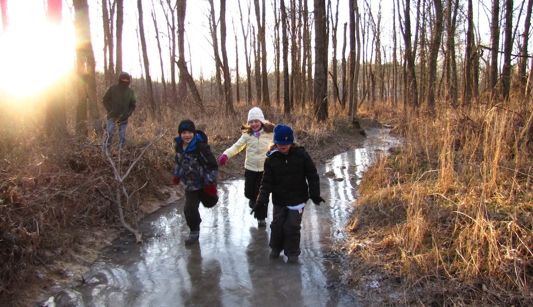 Three children playing on a frozen creek with the sun shining into the lens.
