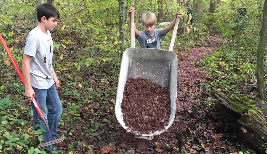 Two young volunteers with a wheelbarrow full of gravel working on trails.