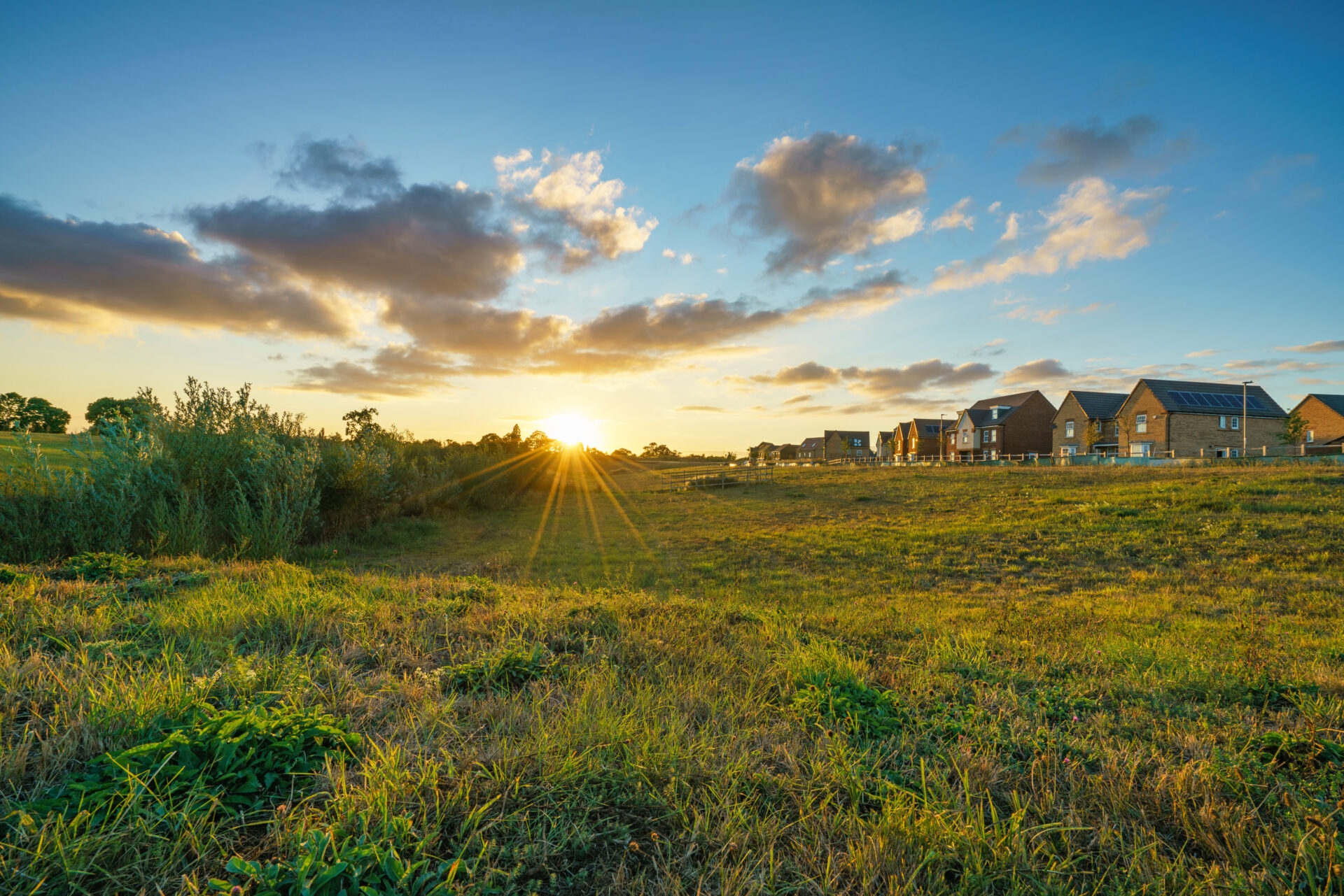 the sun setting over an expansive open field with a stretch of houses on one side