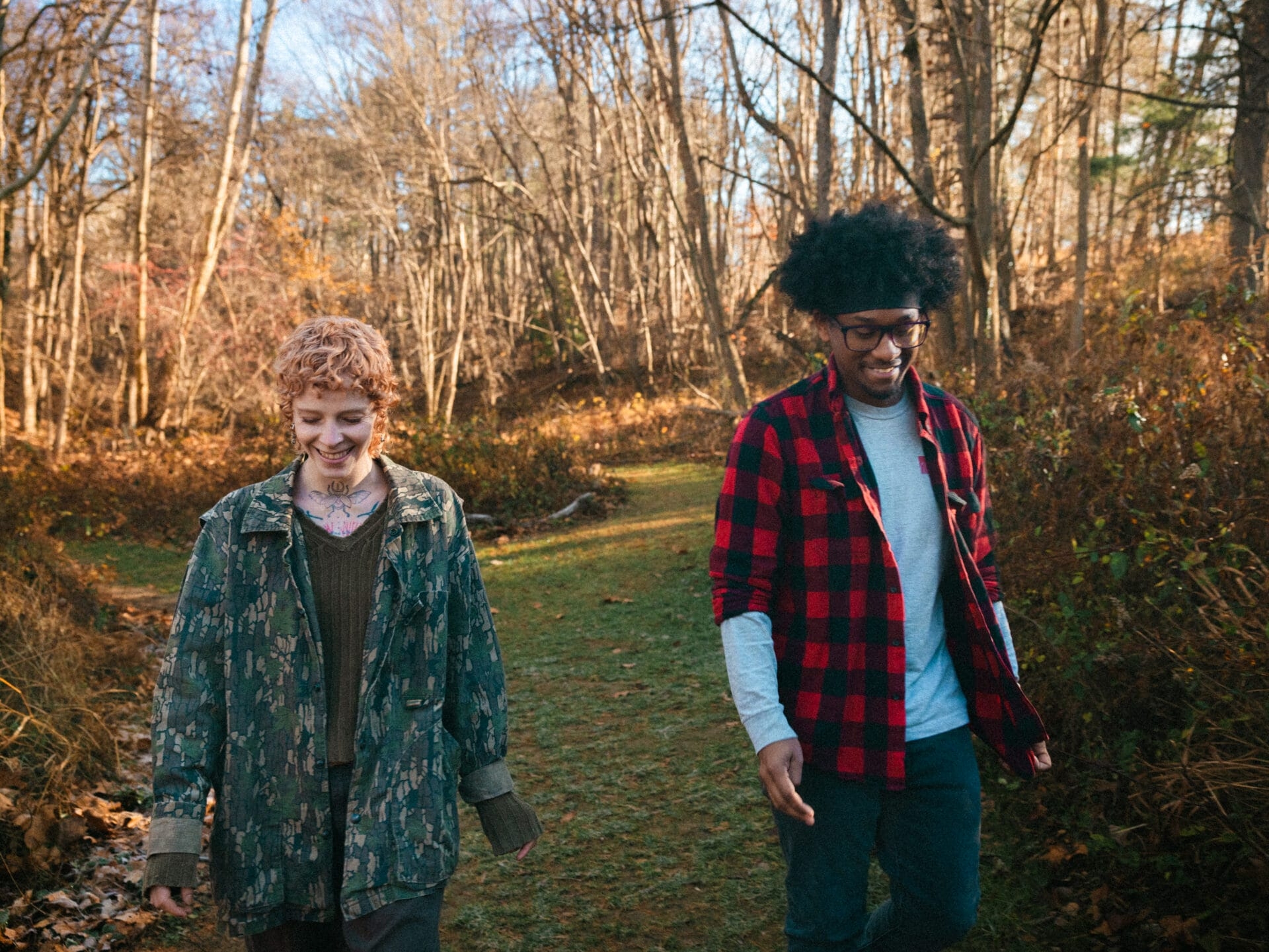 a woman and a man walking along a mown path in the woods in autumn