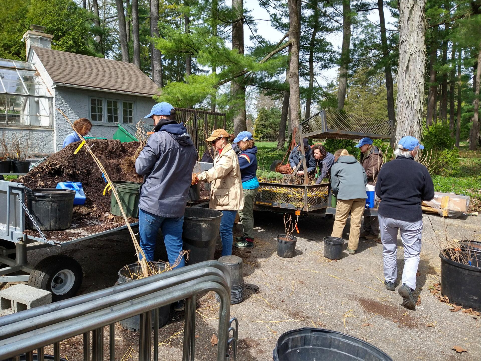 a group of nine people gathered around carts with mulch and potted plants