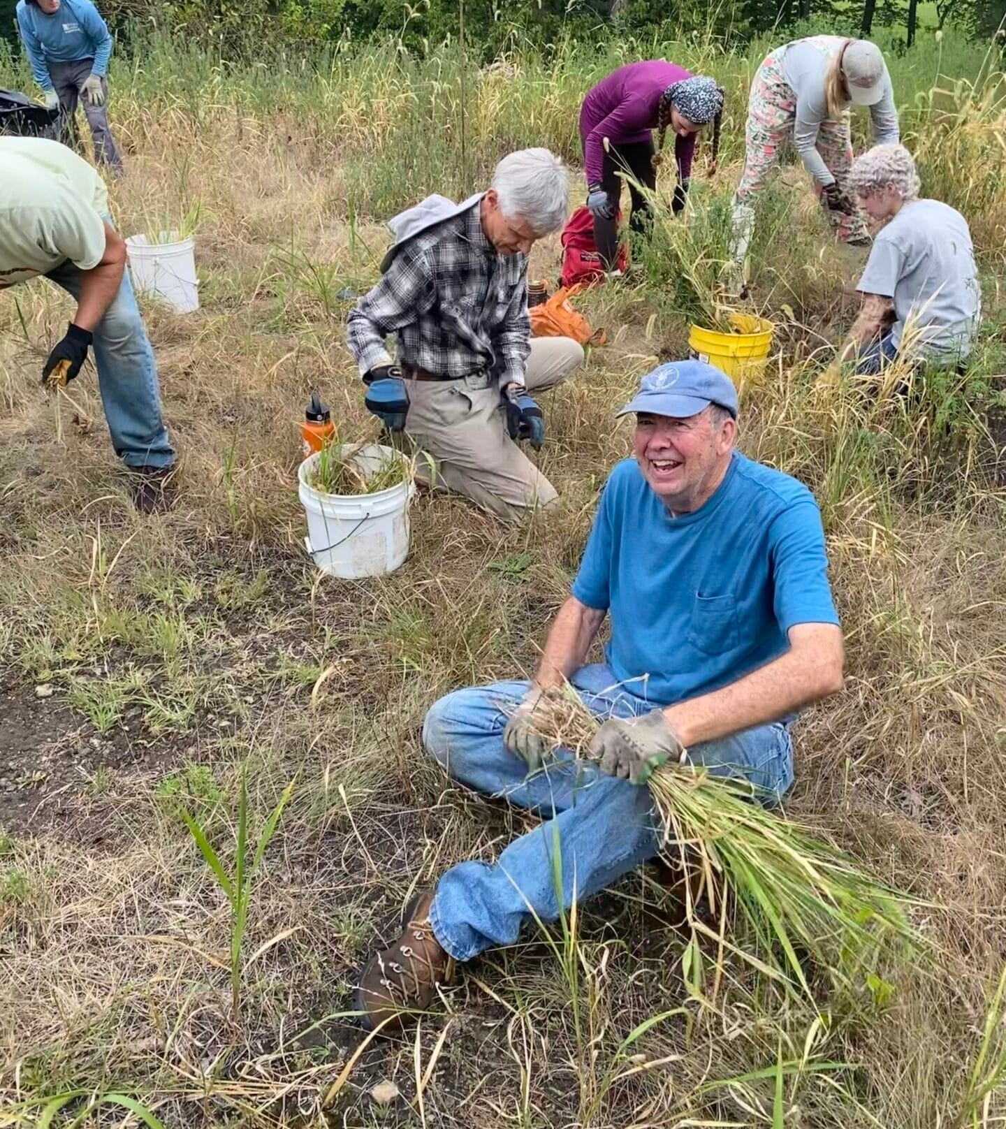 a group of people pulling grasses and a smiling man in foreground
